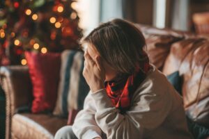 Woman sitting in a room decorated for the holidays, holding her head in her hands.