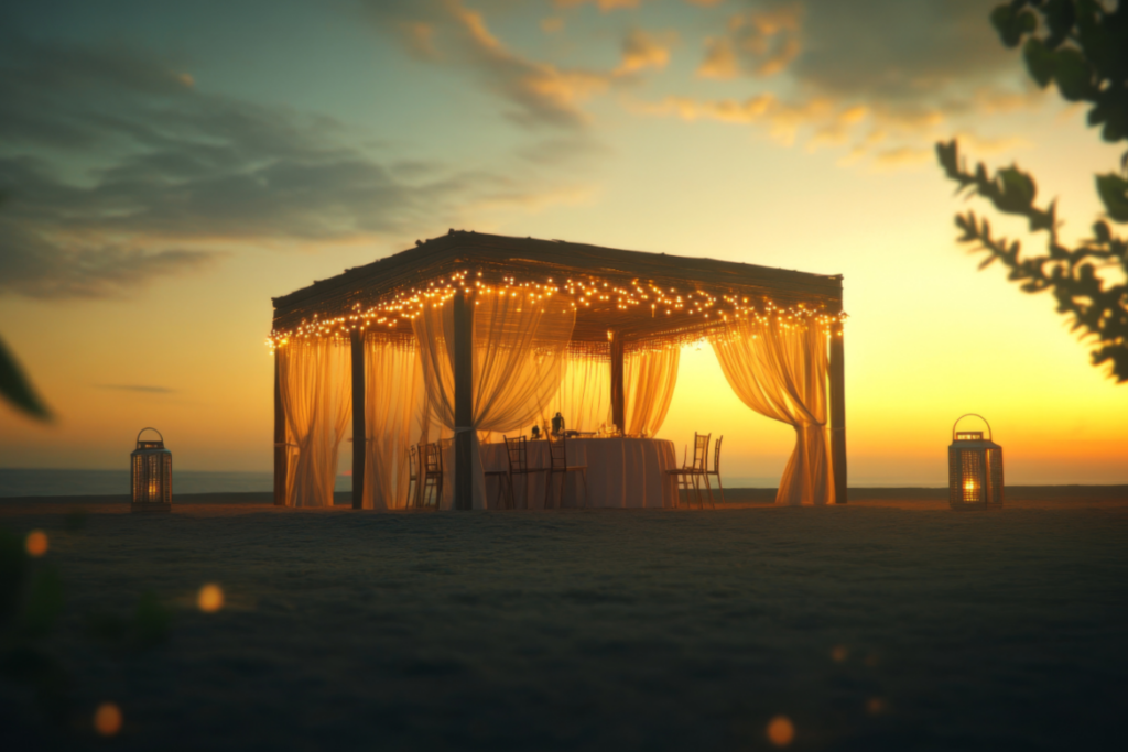 Sukkah decorated with bridal theme on the beach at sunset with two lanterns to the right and left.